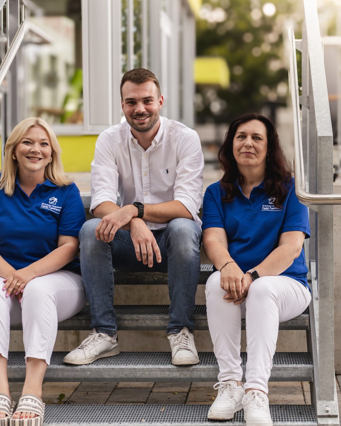 Drei Mitglieder des Kammerer-Teams sitzen auf einer Treppe vor dem Haus